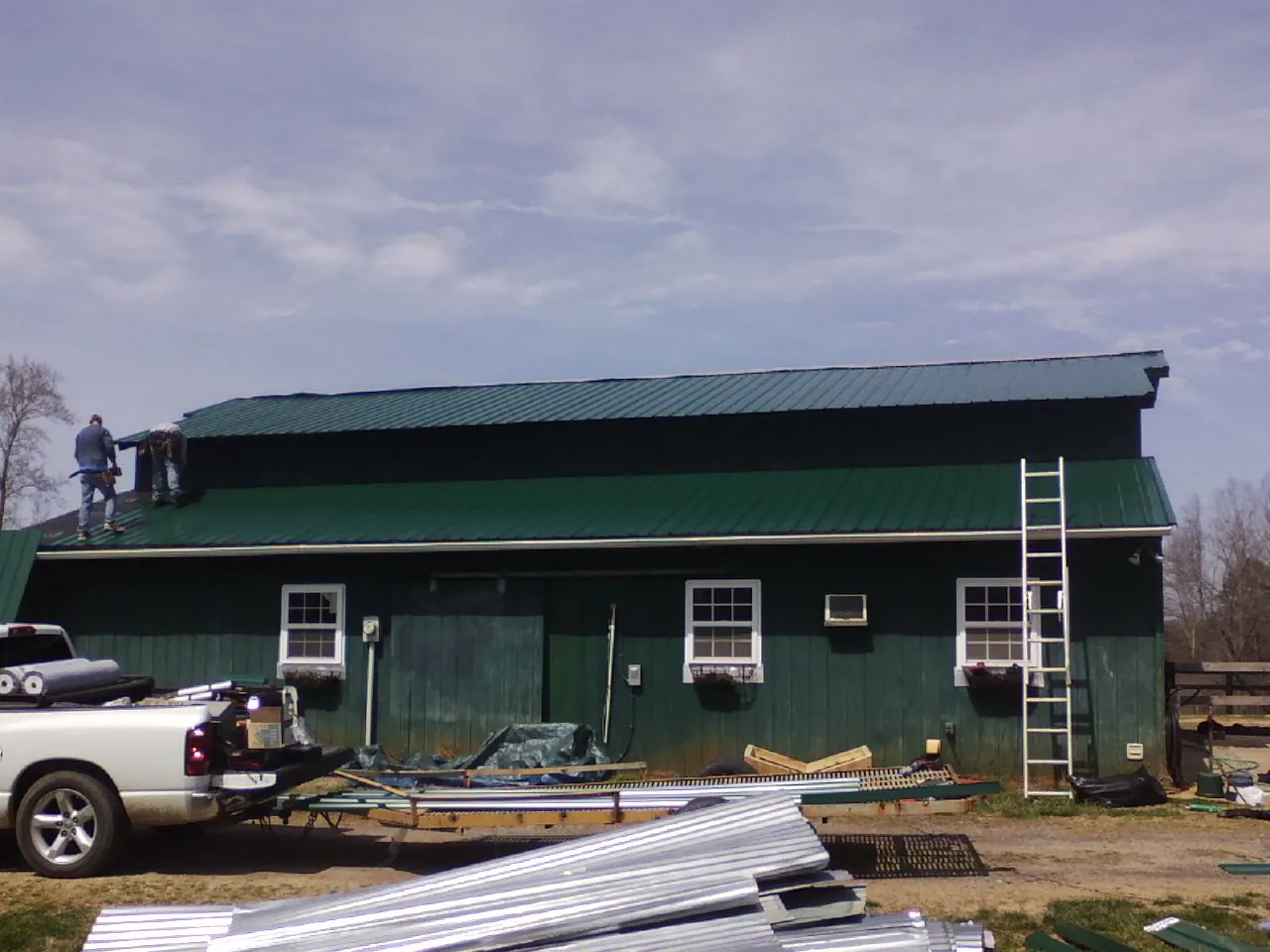 Crew installing green metal roofing on a large green barn in Union